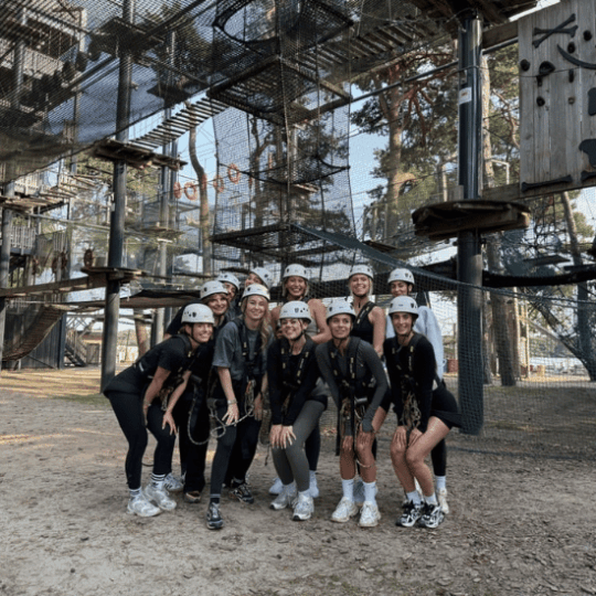11 colleagues going climbing in an adventure park during a team outing. They are posing in the photo wearing harnesses and helmets.