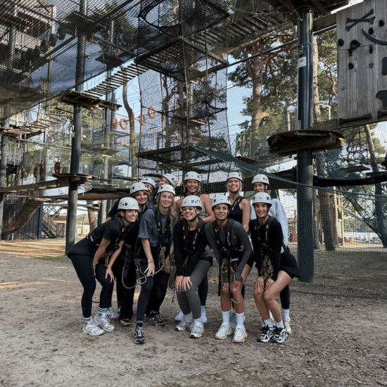 11 collega's die met een teamuitje gaan klimmen in een klimpark. Ze staan op de foto met harnas en helm