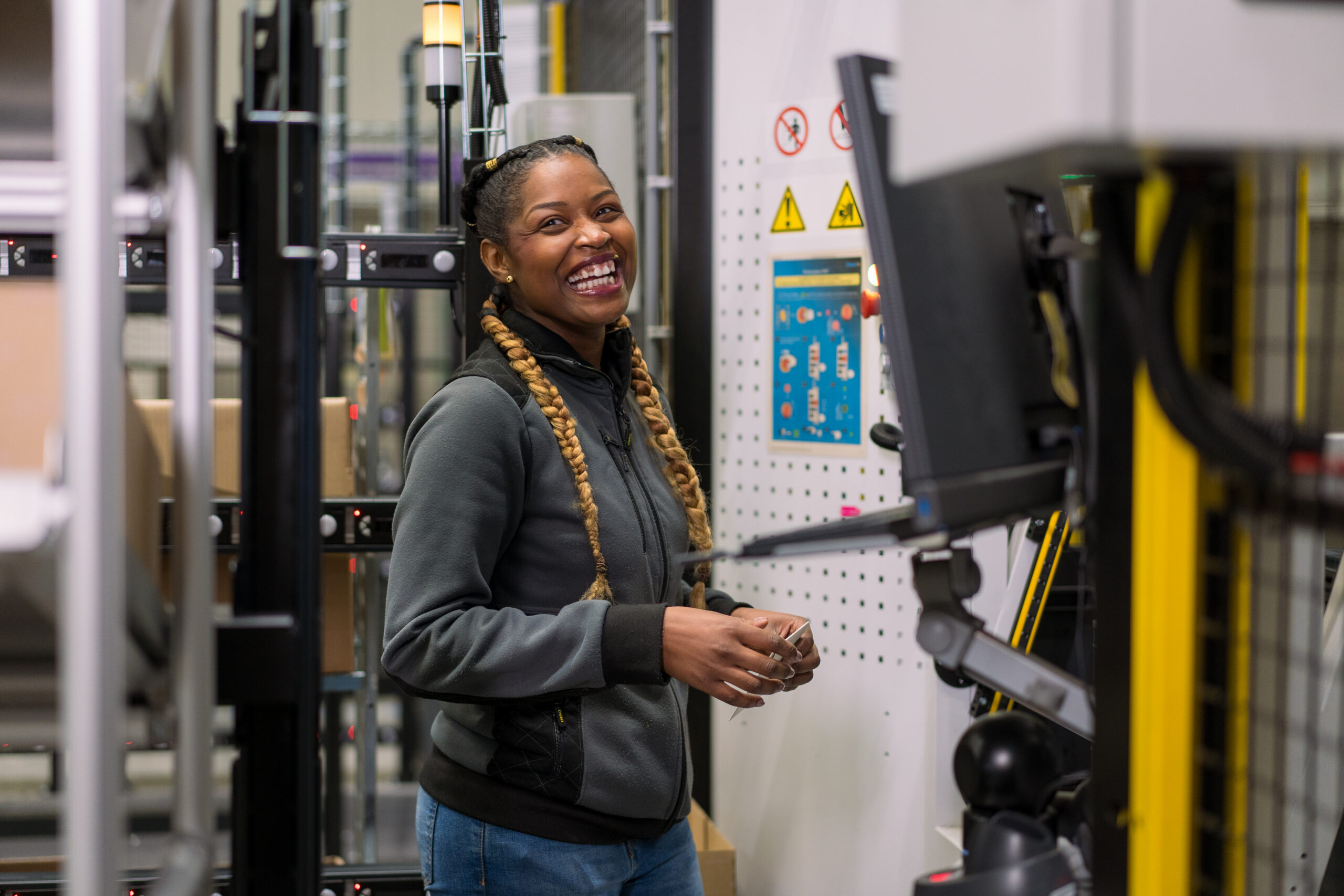 Lachende logistiek medewerker in My Warehouse, het magazijn van My Jewellery, die orders aan het picken is bij de Geek+ robots en lachend richting de camera kijkt