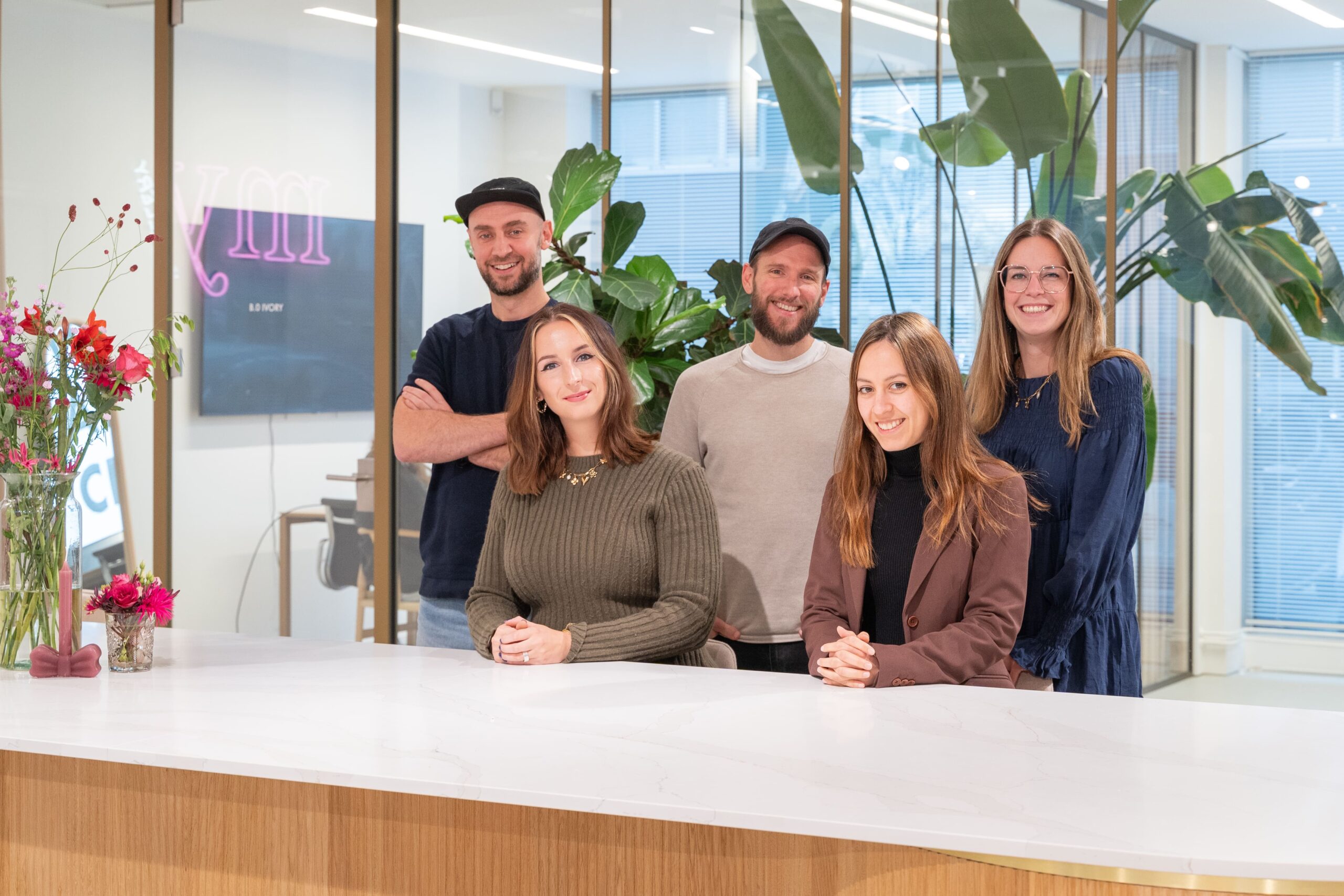 Groepsfoto van het Front-end Development team op het Hoofdkantoor van My Jewellery in 's-Hertogenbosch. Drie vrouwen en twee mannen staan achter een witte balie en kijken lachend de camera in.