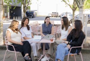 Groepsfoto van het E-mailmarketing team op het Hoofdkantoor van My Jewellery in 's-Hertogenbosch. Vijf vrouwen zitten buiten op roze stoelen aan een roze tafel te lachen naar elkaar.