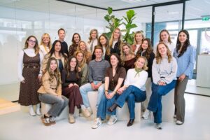 Groepsfoto van het Sales team op het Hoofdkantoor van My Jewellery in 's-Hertogenbosch. Er staan en zitten twintig mensen in een meetingruimte en kijken allemaal lachend de camera in