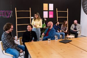 Gruppenfoto des Tech-Teams in der My Jewellery Zentrale in ’s-Hertogenbosch. Sieben Personen befinden sich in der Kantine. Vier Personen stehen vorne links an einem Tisch und unterhalten sich miteinander. Drei Personen sitzen hinten rechts auf bequemen Stühlen und sprechen miteinander.