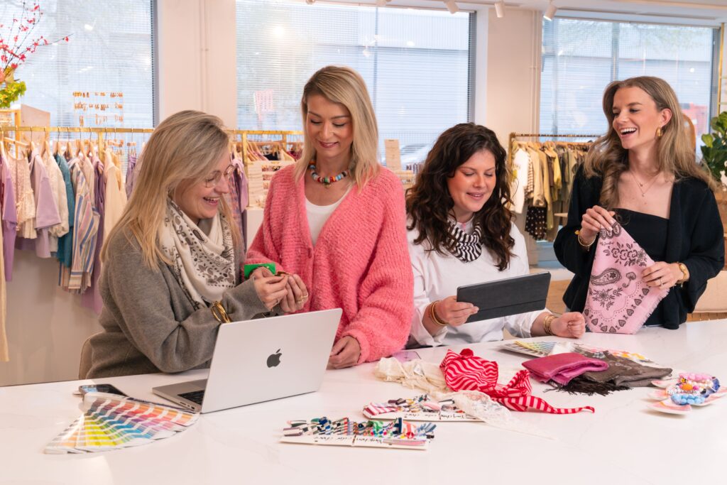 Groepsfoto van het Inkoop (sieraden & accessoires) team op het Hoofdkantoor van My Jewellery in 's-Hertogenbosch. Vier collega's staan in de showroom achter een witte balie waar verschillende items op liggen. Ze zijn aan het overleggen over de items die er liggen en ze in hun handen hebben.