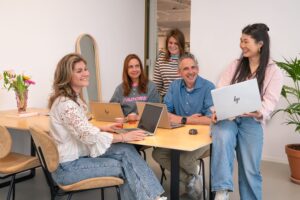 Gruppenfoto des Supply-Chain-Teams in der My Jewellery Zentrale in ’s-Hertogenbosch. Fünf Personen befinden sich in einem Besprechungsraum, davon sitzen drei mit ihren Laptops am Tisch. Eine Person steht dahinter und eine andere sitzt halb auf dem Tisch mit ihrem Laptop.