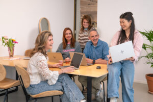 Groepsfoto van het Supply Chain team op het Hoofdkantoor van My Jewellery in 's-Hertogenbosch. Vijf mensen zijn in een meetingruimte, waarvan er drie aan de tafel zitten met laptops. Iemand staat daarachter en de ander zit half op de tafel met haar laptop.