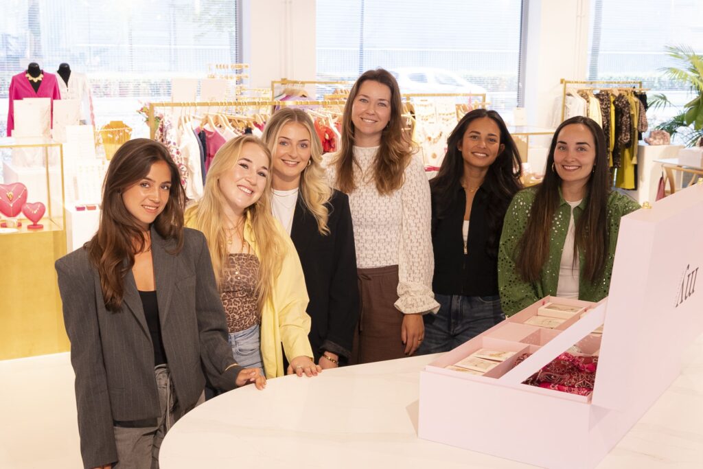 Groepsfoto van het Influencer Marketing team op het Hoofdkantoor van My Jewellery in 's-Hertogenbosch. Zes vrouwen kijken lachend de camera in. Ze staan achter een witte balie waarop een PR-pakket staat