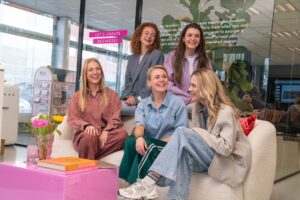 Groepsfoto van het Recruitment team op het Hoofdkantoor van My Jewellery in 's-Hertogenbosch. Er zitten drie vrouwen op een witte bank en twee vrouwen staan erachter. Ze zijn samen aan het praten en lachen naar elkaar