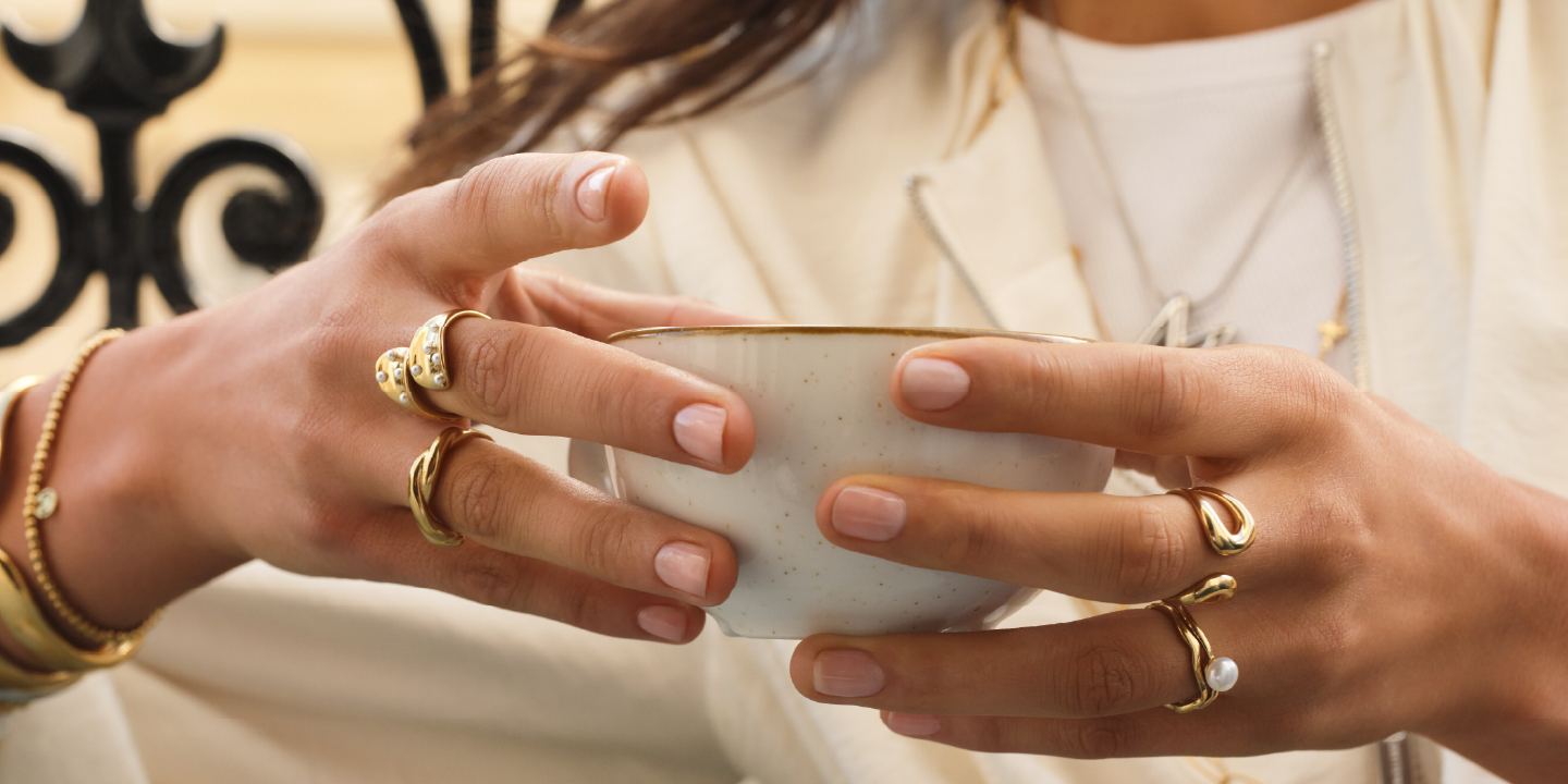 Twee handen met ringen en armbanden die een kopje vasthouden