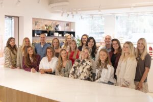 Groepsfoto van het Retail team op het Hoofdkantoor van My Jewellery in 's-Hertogenbosch. Zeventien mensen staan achter een witte balie in de showroom en kijken lachend de camera in