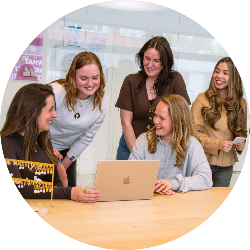 Teamfoto van het Sales Backoffice team op het Hoofdkantoor van My Jewellery in 's-Hertogenbosch. Vijf vrouwen zijn in een meetingruimte en zijn aan het overleggen en lachen. Ze zijn naar een laptop aan het kijken en er staat een sieraden display op tafel.