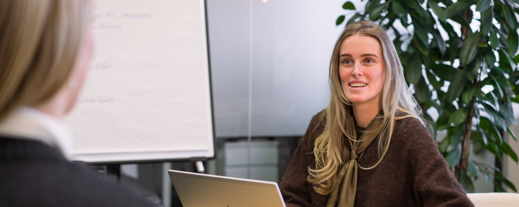 Applicatie beheerder van My Warehouse, het magazijn van My Jewellery, die in een meeting ruimte zit achter haar laptop en in gesprek is met een andere collega