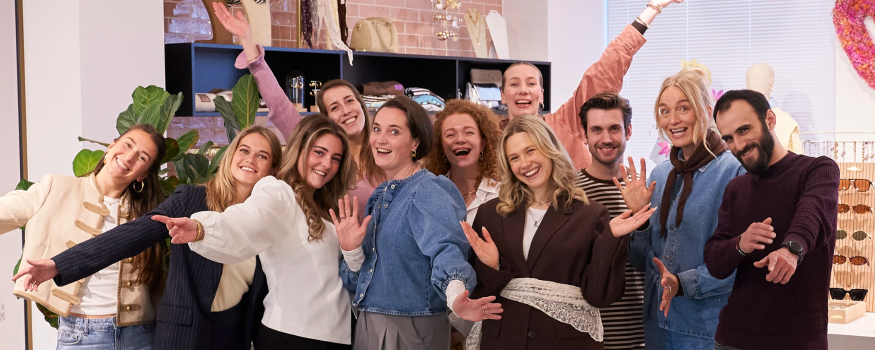 Elf collega's die in de showroom op het My Jewellery Hoofdkantoor in 's-Hertogenbosch staan en lachen naar de camera. Ze hebben hun armen in de lucht en kijken erg vrolijk.