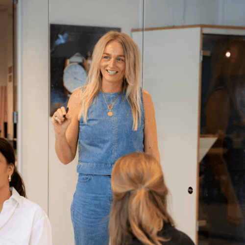 A colleague in a meeting room talking with colleagues while holding a pen in her hand.