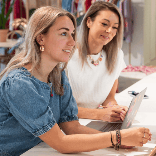 Two Buying colleagues with a laptop in the showroom surrounded by clothing. Smiling colleagues looking at the laptop.
