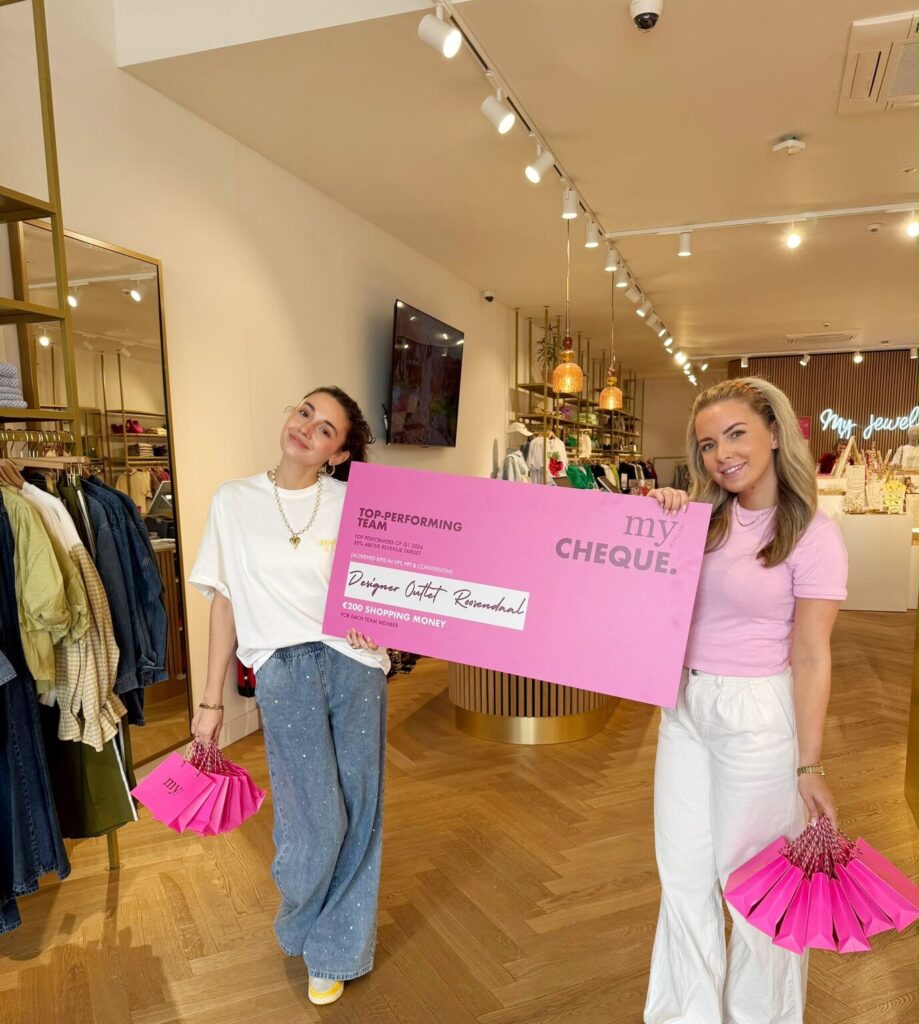 Deux femmes de la boutique My Jewellery du Designer Outlet Roosendaal sourient à la caméra, un chèque rose à la main