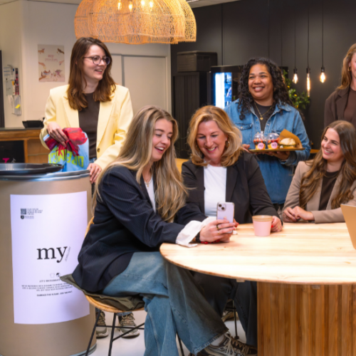 Groepsfoto van het Facilities team op het Hoofdkantoor van My Jewellery in 's-Hertogenbosch. Het zijn tien collega's die in de Bistro kantine om een ronde tafel zitten en staan. Ze lachen en overleggen met elkaar