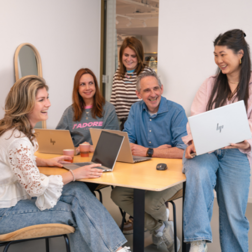 Groepsfoto van het Supply Chain team op het Hoofdkantoor van My Jewellery in 's-Hertogenbosch. Vijf mensen zijn in een meetingruimte, waarvan er drie aan de tafel zitten met laptops. Iemand staat daarachter en de ander zit half op de tafel met haar laptop.