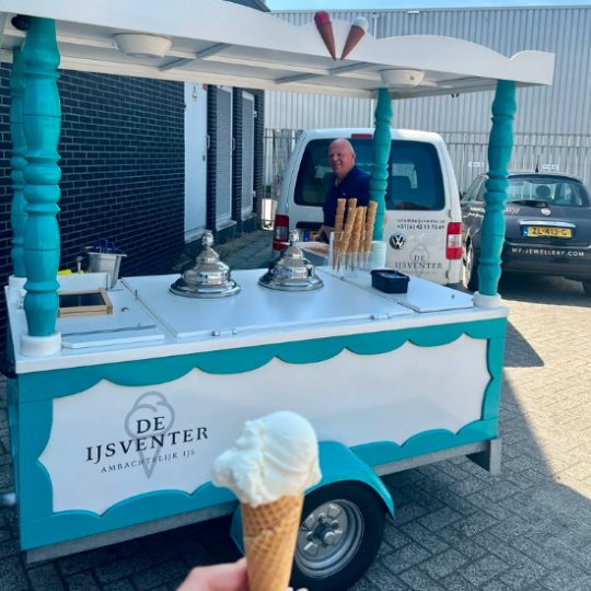 Un homme souriant se tient derrière un chariot à glaces vert et blanc