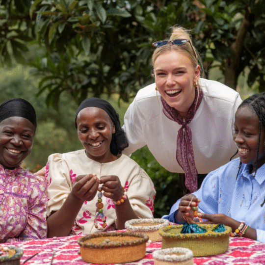 Een My Jewellery-collega maakt samen met drie vrouwen kleurrijke armbanden aan een tafel buiten voor Jukumu Letu in Kenia.